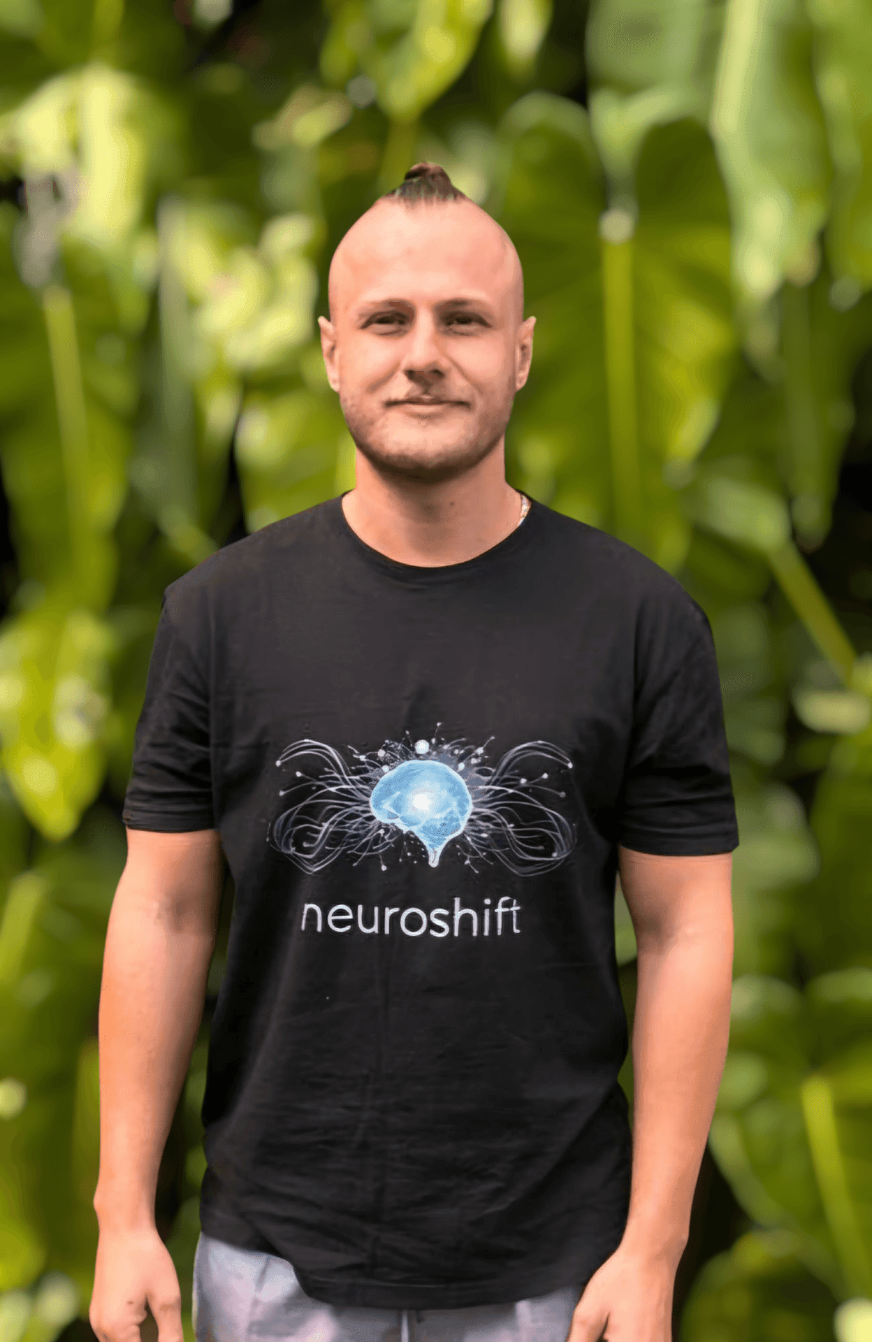 Person wearing a black 'neuroshift' T-shirt stands in front of lush green leaves.